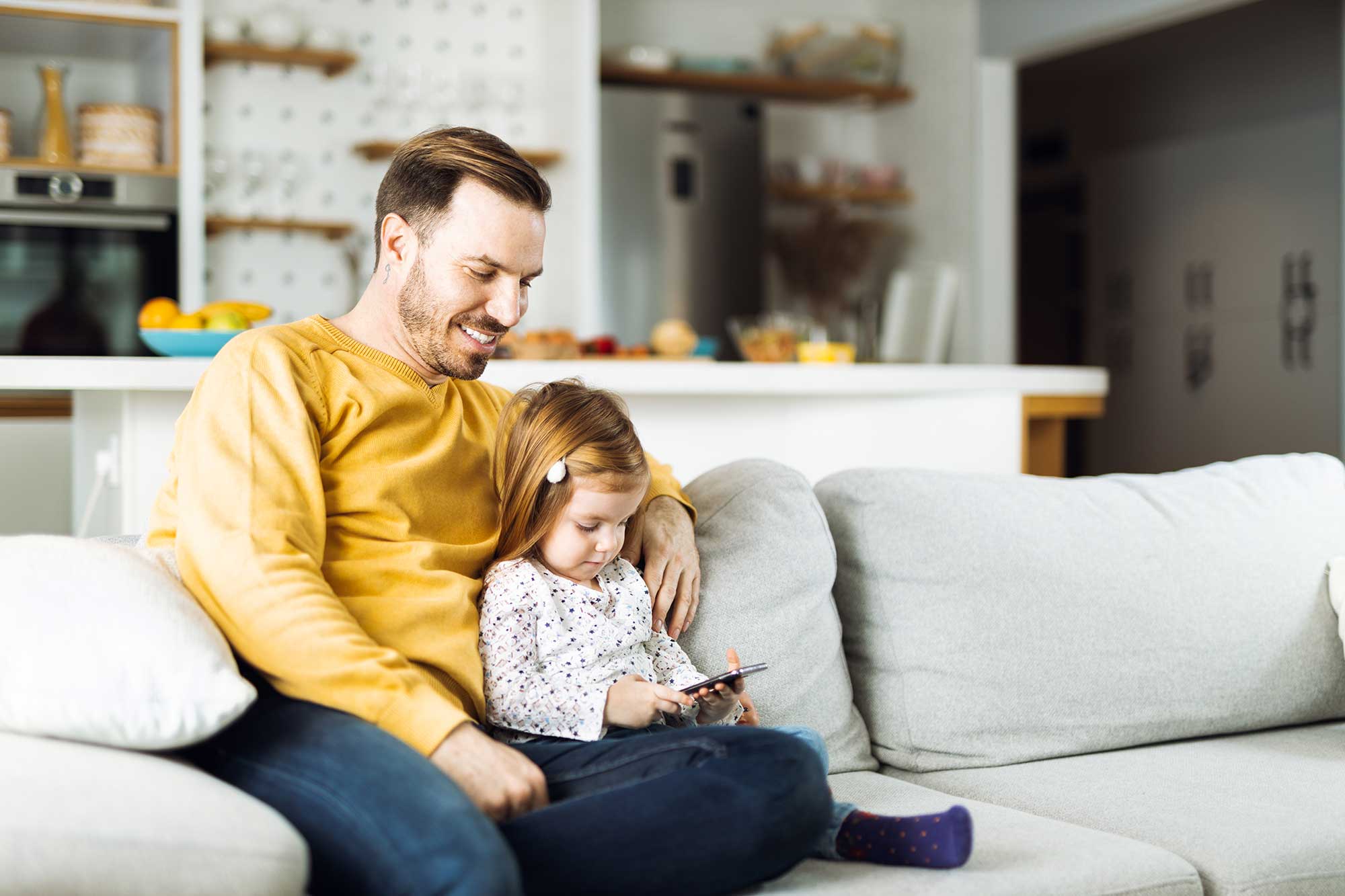 Pappa och dotter sitter i soffa med mobiltelefon