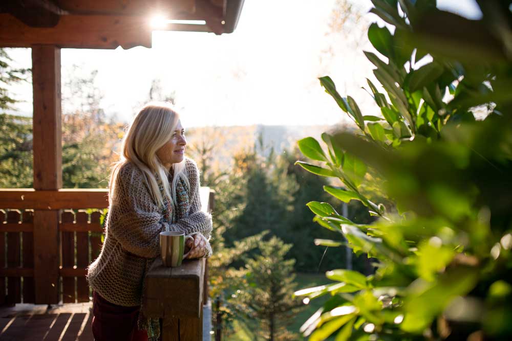 Kvinna står på en veranda omgiven av växter och ser beskymmersfri ut.